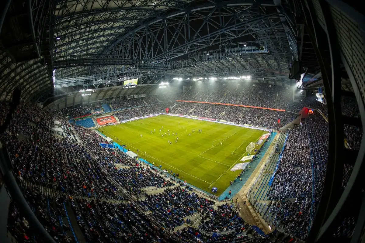 Stadion Lecha Poznań wypełniony kibicami, zielona murawa, mecz piłki nożnej. Pojemność stadionu robi wrażenie.