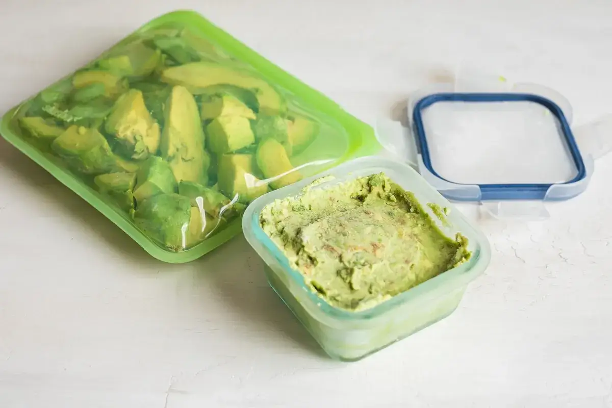 Avocado in Stücken in einem wiederverwendbaren Beutel und Guacamole in einem Behälter. So kann man Avocado einfrieren und Lebensmittelverschwendung vermeiden.