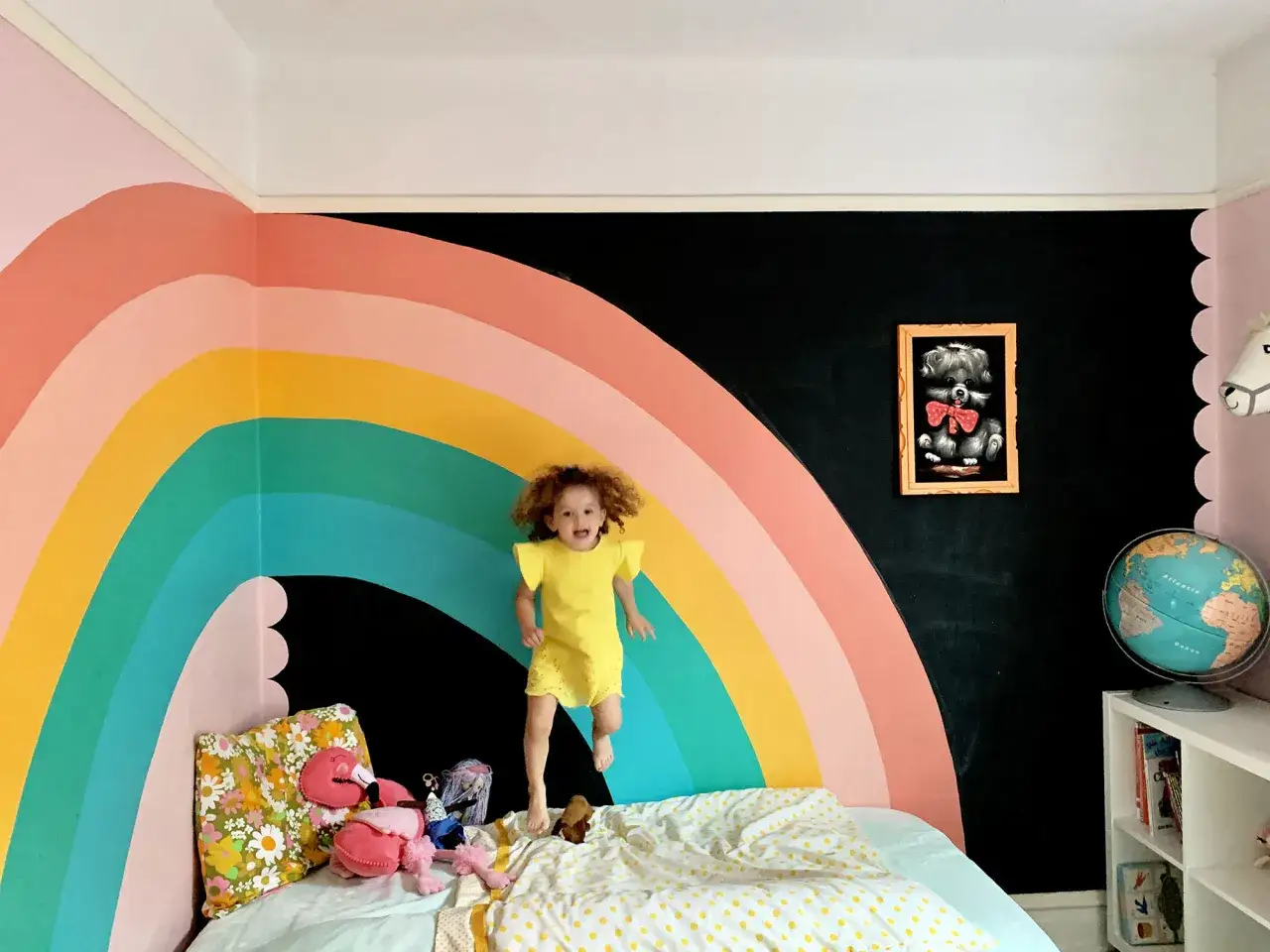 Une petite fille saute sur un lit devant un mur o&ugrave; l'on peut peindre un arc en ciel.