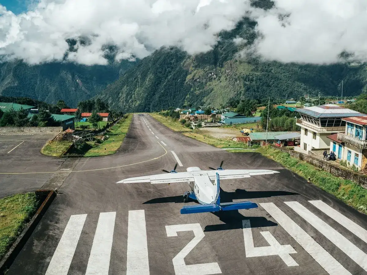 Samolot na pasie startowym lotniska w Nepalu, znanego jako najniebezpieczniejsze lotnisko na świecie. Góry i chmury w tle.