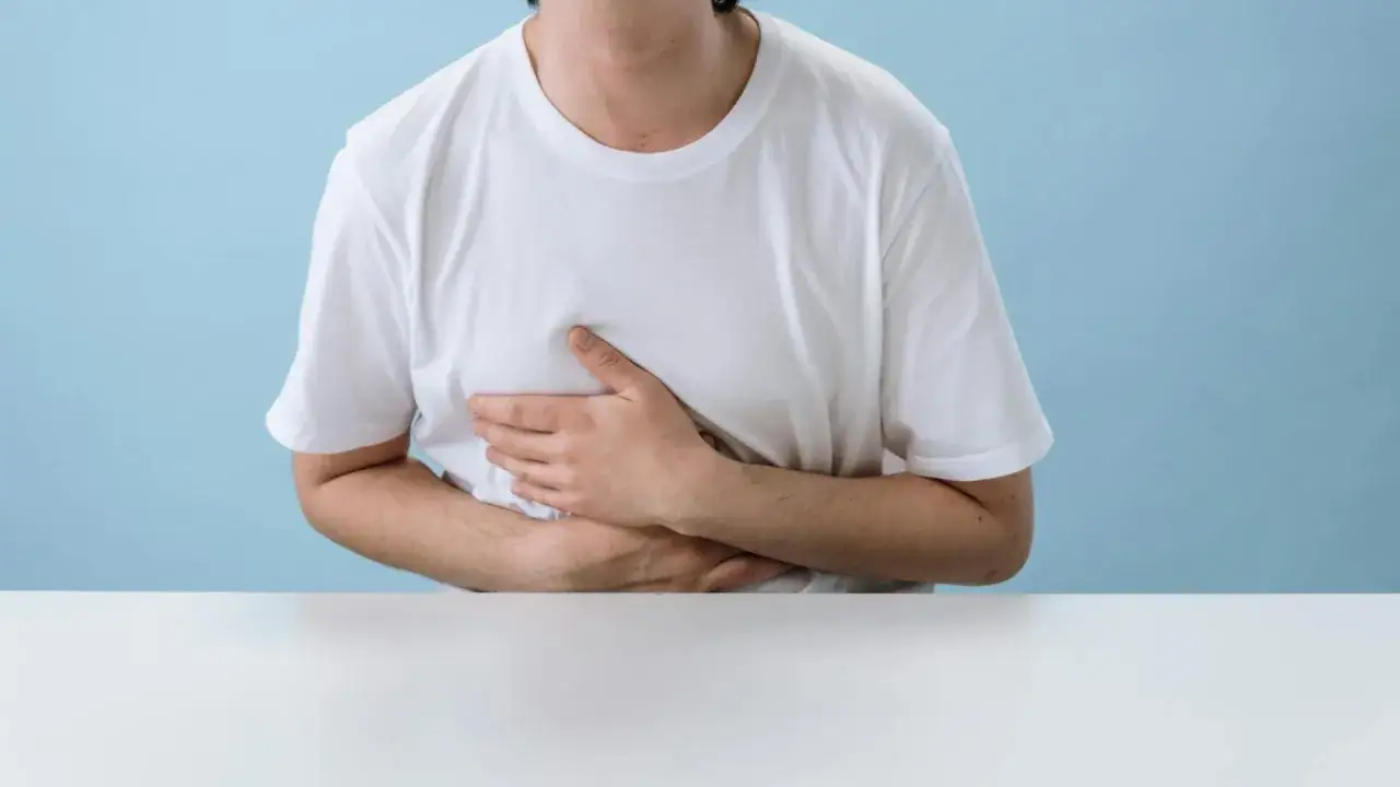 Uomo con mani sull'addome, preoccupato per possibili sintomi come ansia e sangue nelle feci.