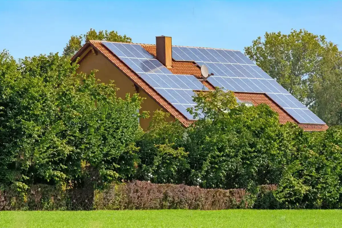 Casa verde in Europa con pannelli solari sul tetto, circondata da alberi rigogliosi e un prato curato.