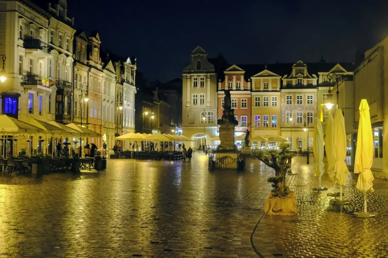 Nocny Rynek w Poznaniu, z mokrym brukiem odbijającym światła latarni i kolorowych kamienic. Idealne miejsce na wieczorne poznańskie atrakcje dla dorosłych.