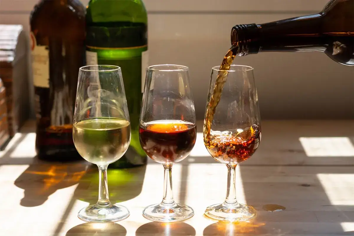 Drei Gläser mit Sherry Aperitif, eines wird gerade nachgefüllt.