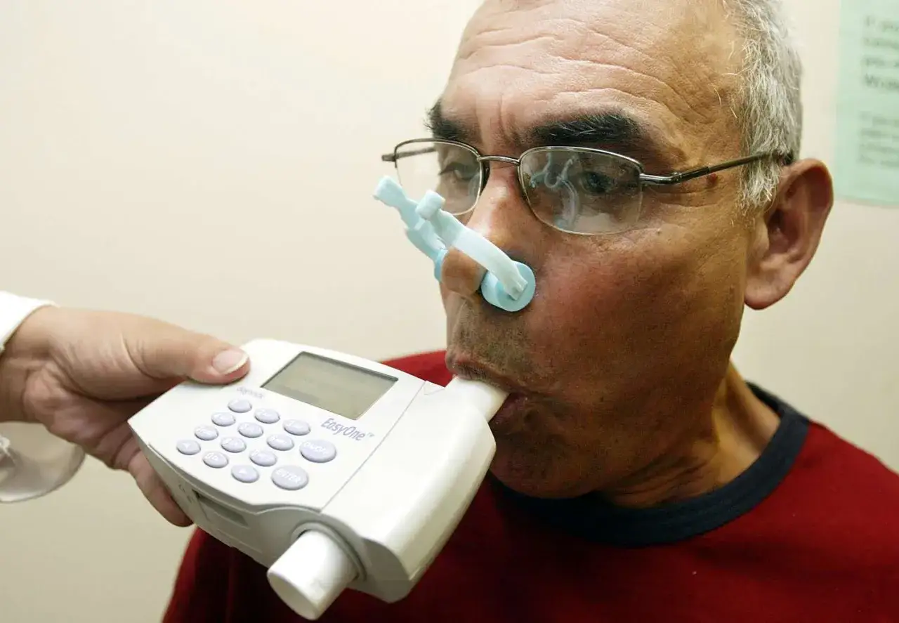 Mann mit Nasenklemme und Mundst&uuml;ck f&uuml;r Lungenfunktionstest. Ein Arzt h&auml;lt das Ger&auml;t, um die Lungenkapazit&auml;t zu messen, vielleicht nach der Anwendung von Asthmaspray.