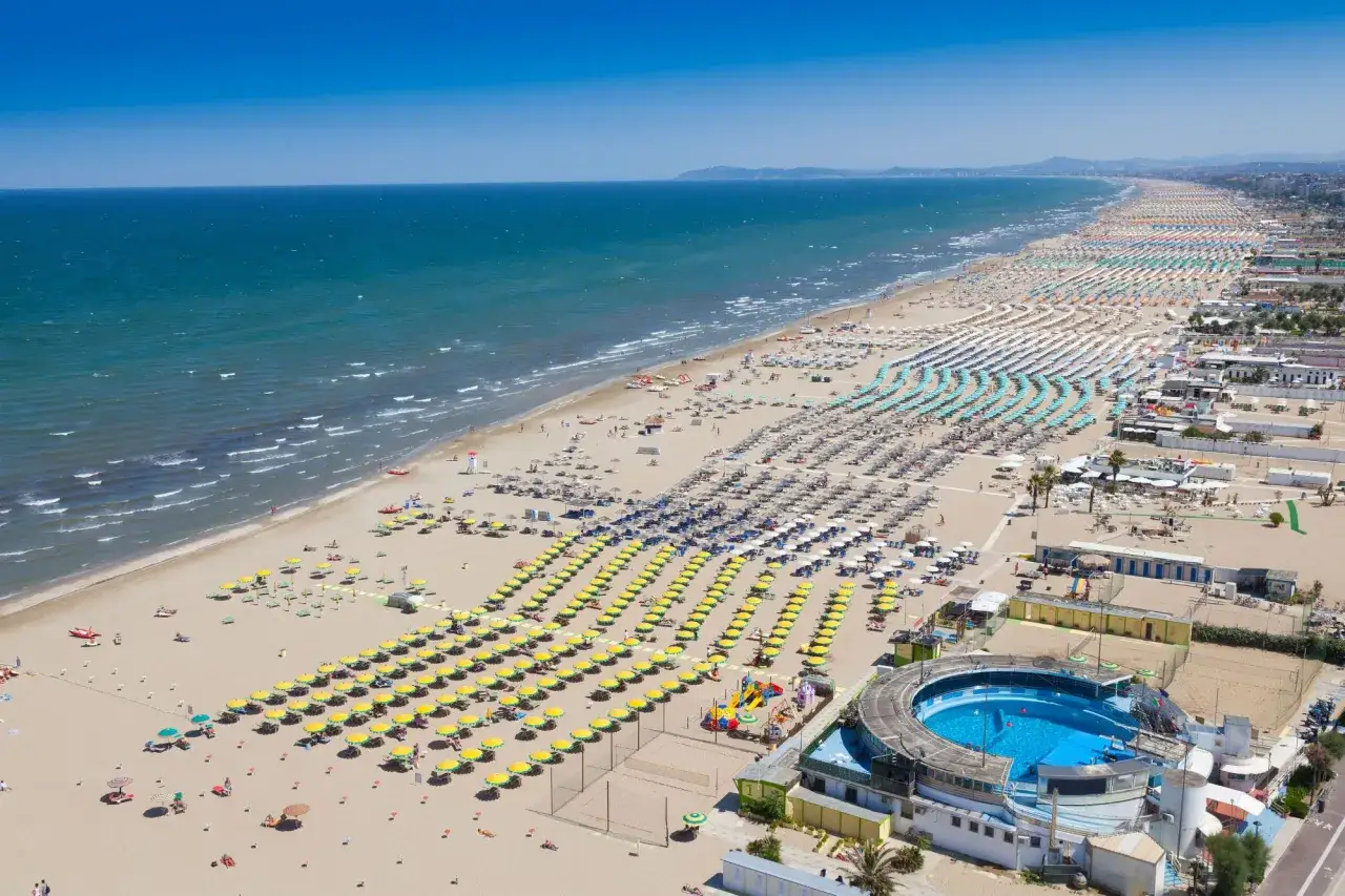 Słoneczna Rimini plaża z rzędami parasoli i leżaków, błękitne morze i basen z wodą.