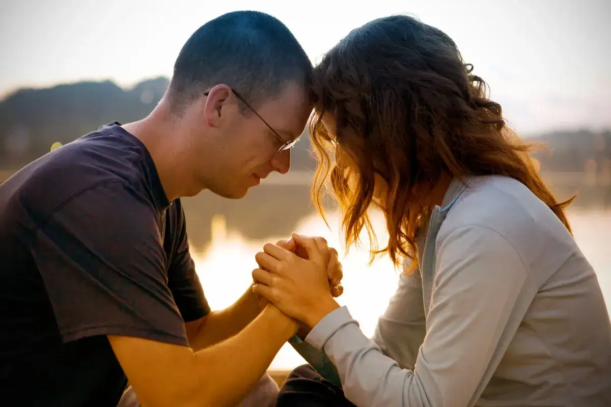 Un couple uni dans la pri&egrave;re des &eacute;poux, front contre front, mains jointes, partageant un moment de foi et d'amour au coucher du soleil.