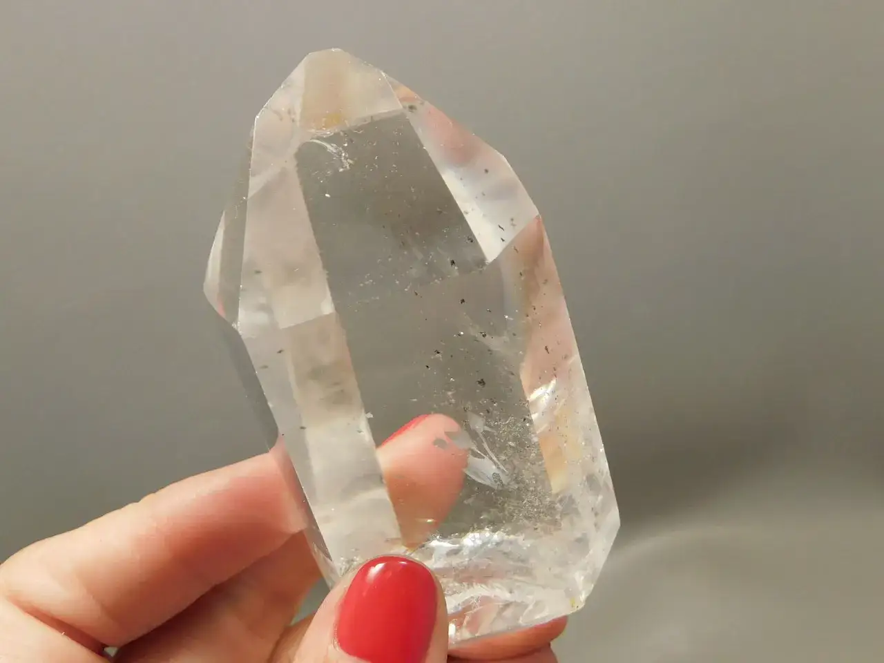 En hand med rött nagellack håller en stor, klar bergkristall. Denna bergkristall, även känd som