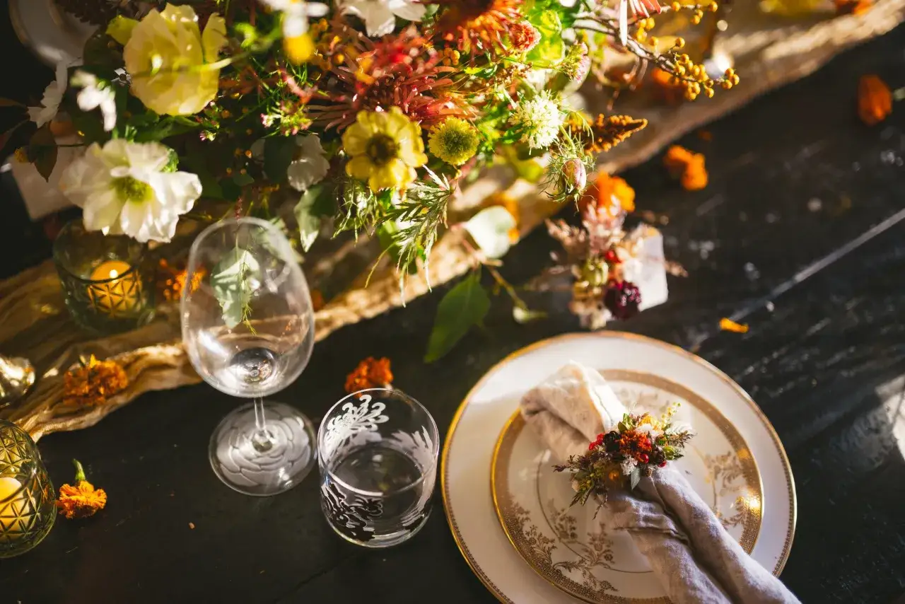 Une table dressée pour un mariage bohème, avec un bouquet champêtre, des bougies et un pliage serviette mariage bohème orné de fleurs séchées.