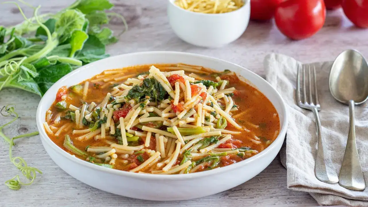 Un piatto fumante di pasta con i tenerumi asciutta, arricchita da pomodoro fresco e verdure.