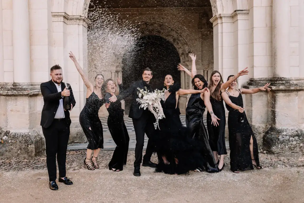 Un groupe joyeux célèbre un mariage noir et blanc, le marié ouvrant une bouteille de champagne tandis que les demoiselles d'honneur crient de joie.