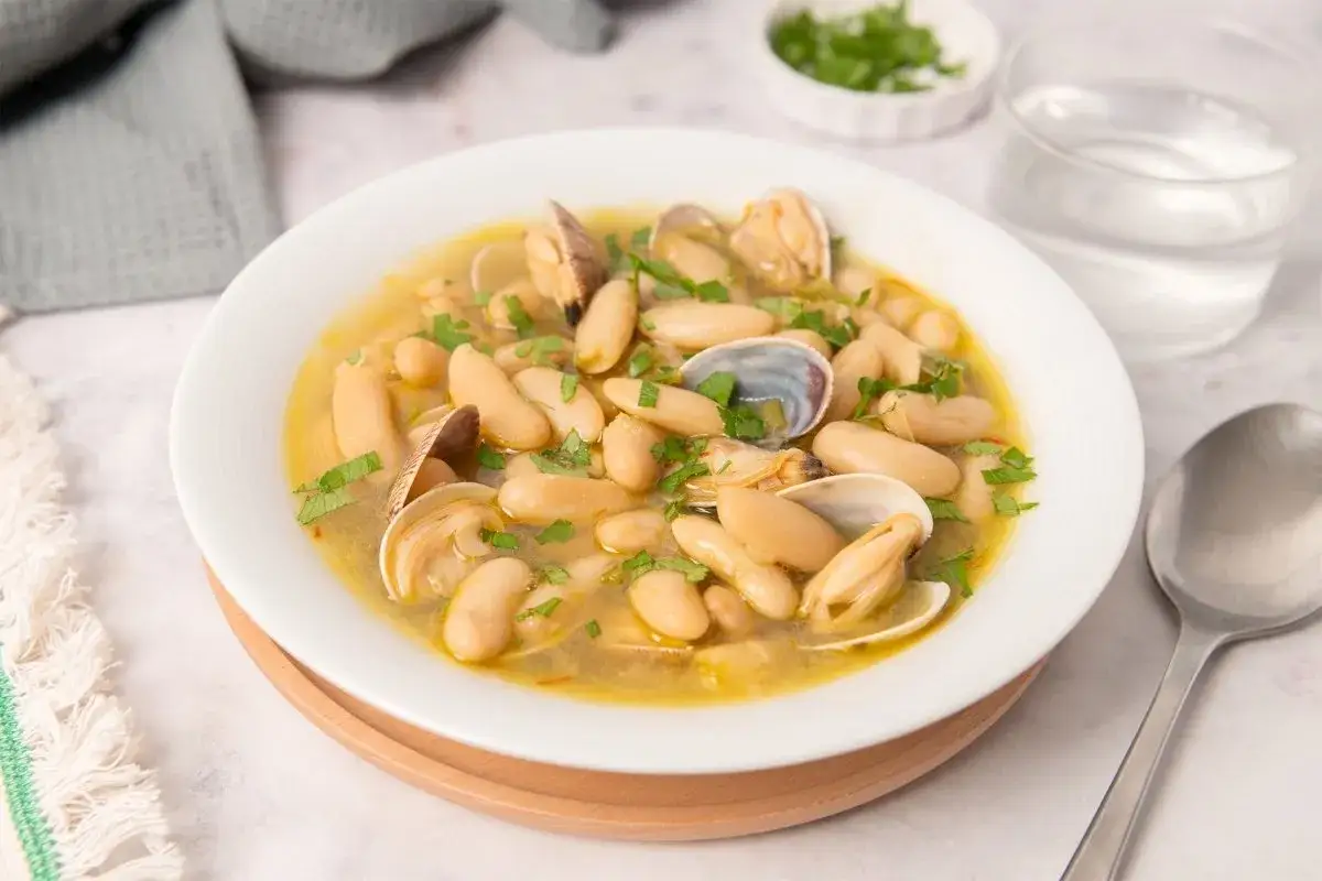Plato de habichuelas con almejas, un guiso reconfortante con judías blancas tiernas y almejas frescas, espolvoreado con perejil picado.