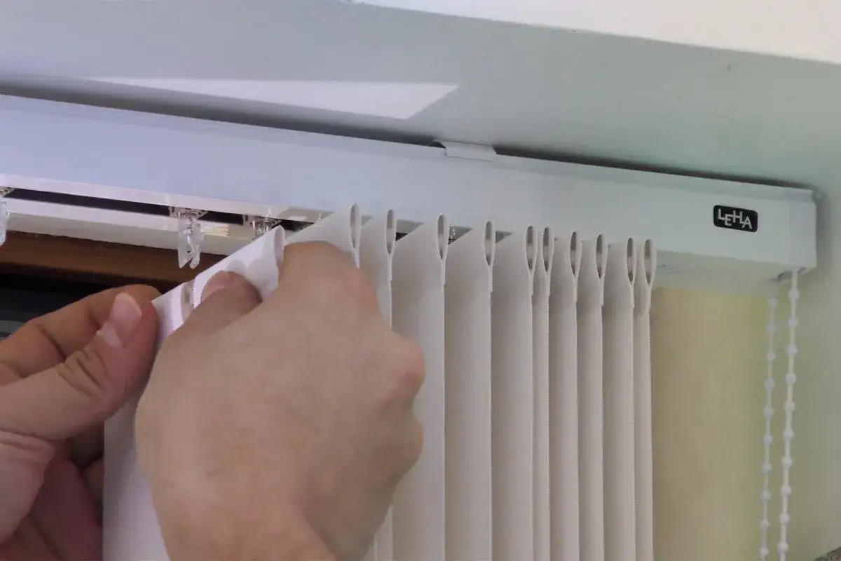 H&auml;nde befestigen einen wei&szlig;en Lamellenvorhang in einer Gardinenschiene. Die Lamellen werden in kleine Clips an der Schiene eingeh&auml;ngt.