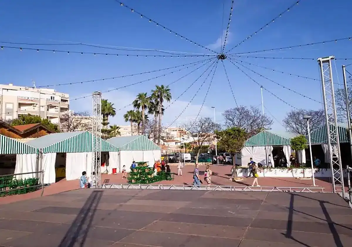 Puestos de la feria Torrevieja bajo un cielo azul, con toldos a rayas verdes y blancas y luces colgantes.