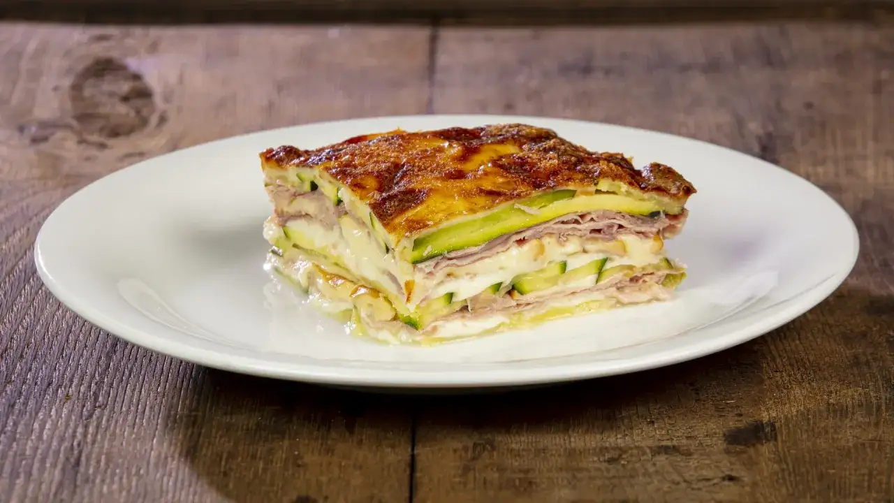 Una fetta di parmigiana di zucchine bianca alla napoletana, stratificata con prosciutto e formaggio, su un piatto bianco.