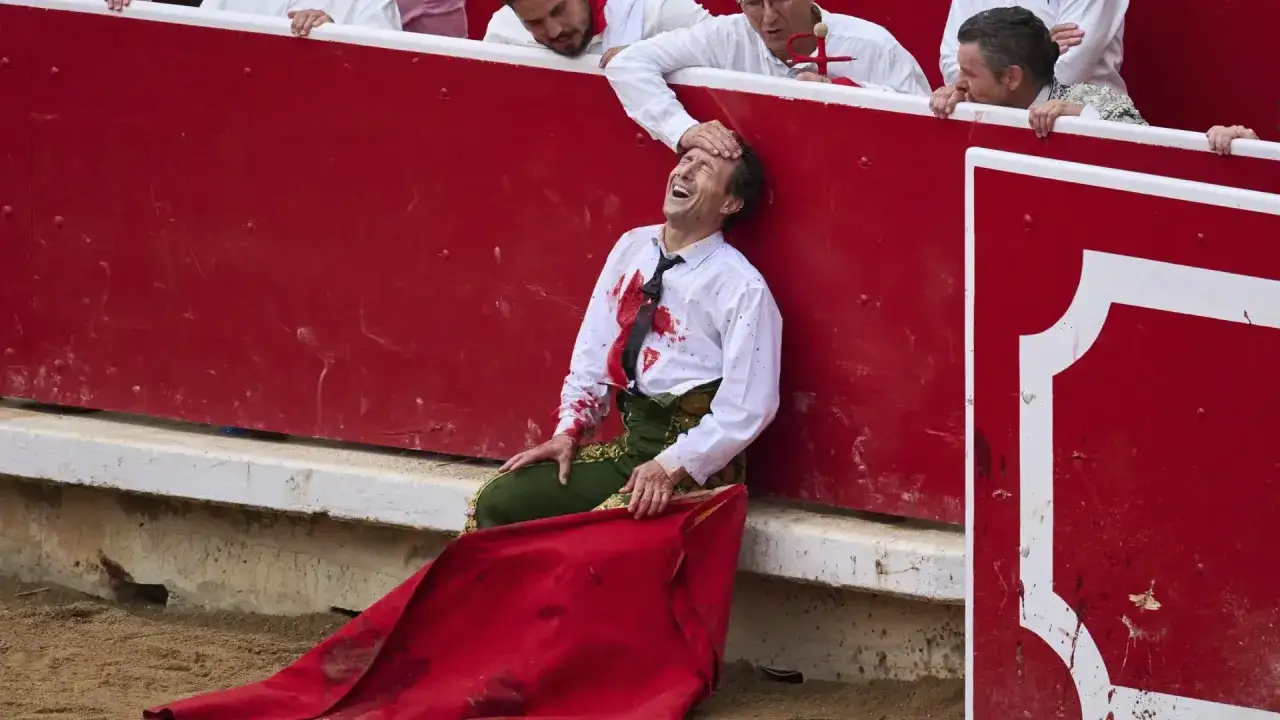 Rafaelillo torero, herido y con la camisa manchada de sangre, se apoya en la barrera roja mientras otros lo observan.