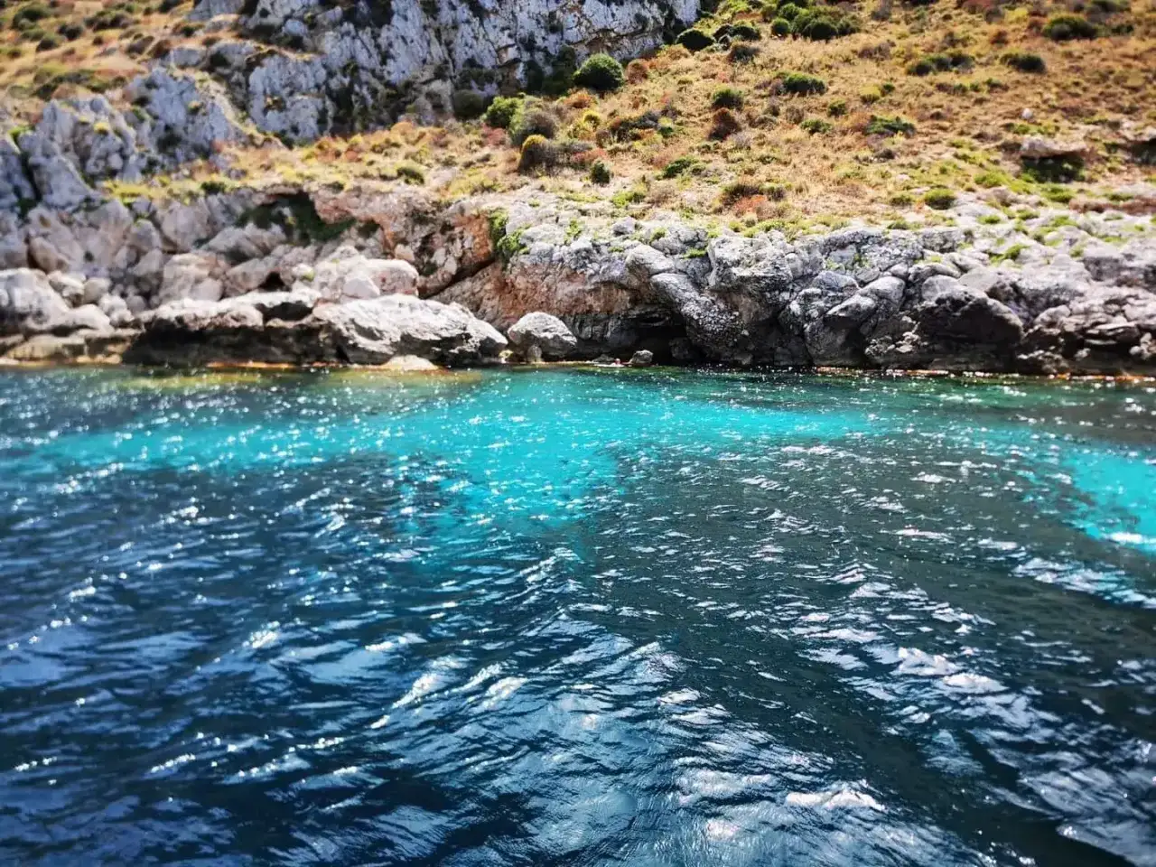 Acque cristalline del mare di Favignana, con rocce scoscese e vegetazione mediterranea che si tuffano nel blu intenso.
