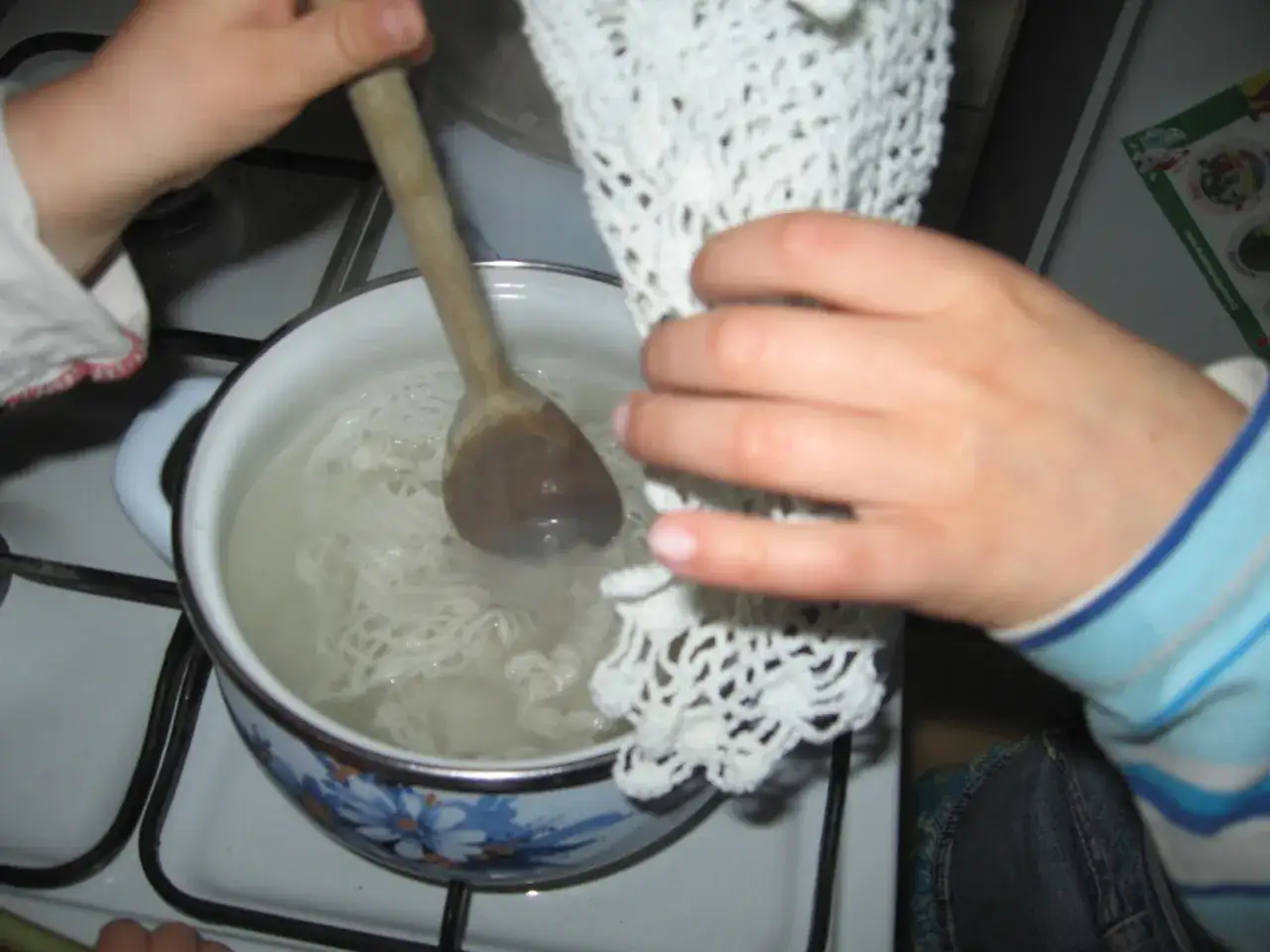Dziecko miesza drewnianą łyżką koronki w garnku z wodą, przygotowując się do tego, jak zrobić krochmal.