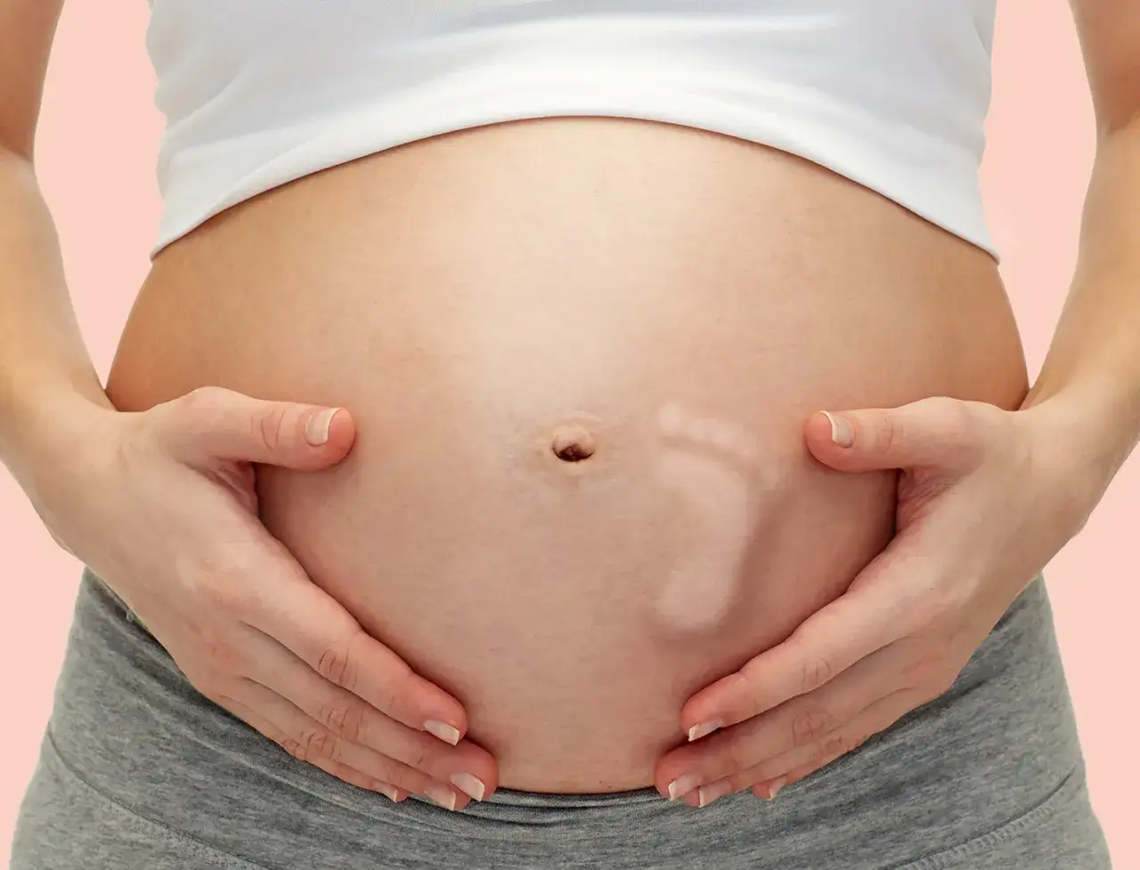 Brzuszek w 29 tygodniu ciąży, z widocznym odciskiem st&oacute;pki dziecka. Ręce mamy delikatnie obejmują rosnący brzuch.