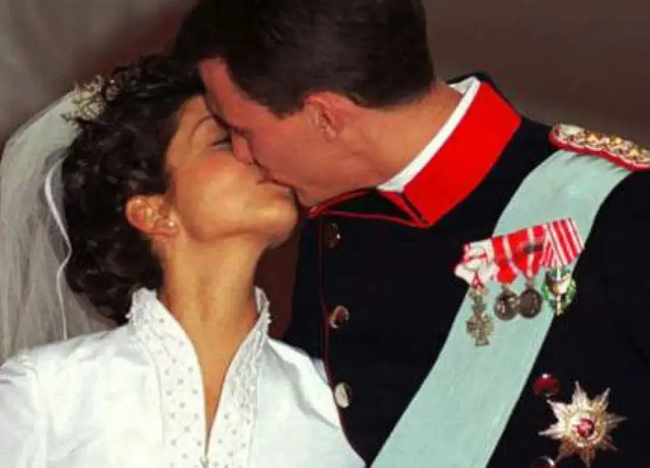 Alexandra, grevinna av Frederiksborg, kysser sin make p&aring; deras br&ouml;llopsdag. Hon b&auml;r en vit kl&auml;nning och sl&ouml;ja, han en milit&auml;runiform med ordnar.