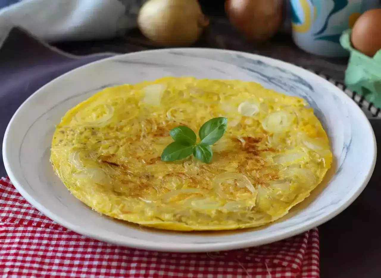 Frittata di cipolle dorata e soffice, guarnita con una fogliolina di basilico, su un piatto bianco.