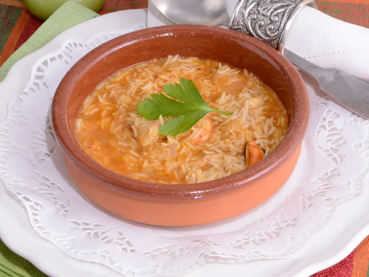 Sopa de pescado con arroz sencilla, servida en cuenco de barro, con mejillones y gambas, decorada con perejil.