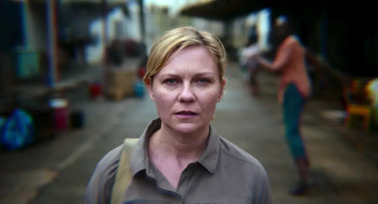 Kirsten Dunst w filmach, zamyślona, w szarym ubraniu, na tle rozmytego, miejskiego krajobrazu.
