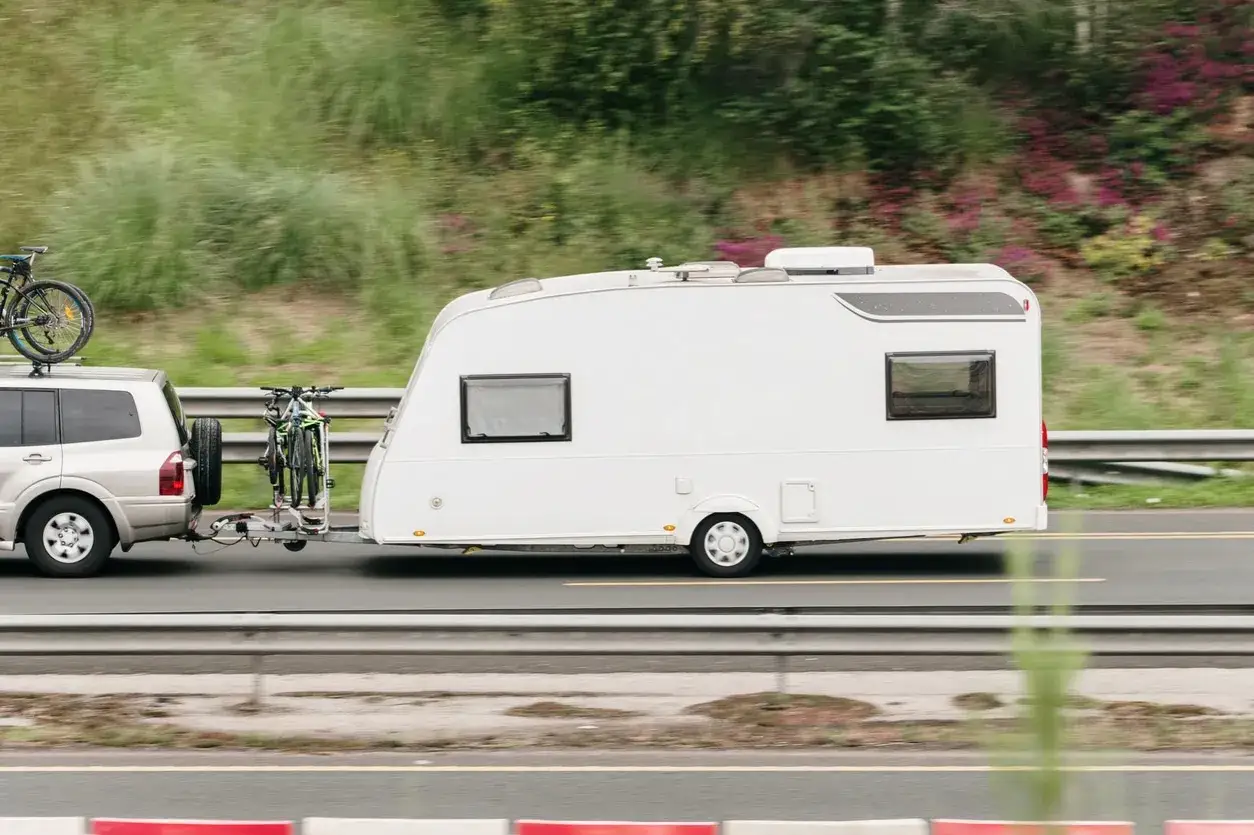 Un coche remolca una caravana por la carretera, con bicicletas en la baca y en un portabicicletas. Ideal para quienes tienen el carnet de conducir B2 y disfrutan de viajes largos.
