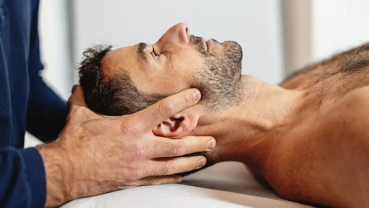 Delikatne dłonie terapeuty wykonują terapię cranio sacralną, przykładając nacisk na głowę i szyję pacjenta.