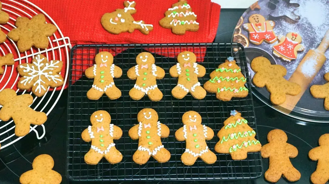 Galletas de jengibre decoradas con glaseado blanco y verde, con formas de hombrecitos, árboles y copos de nieve.