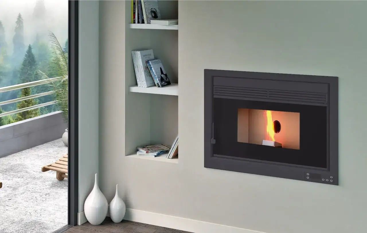 Chimenea moderna empotrada en la pared, con fuego encendido y lista para insertar pellets. A la izquierda, una estanter&iacute;a con libros y una puerta corredera que da a un balc&oacute;n con vistas a un bosque.