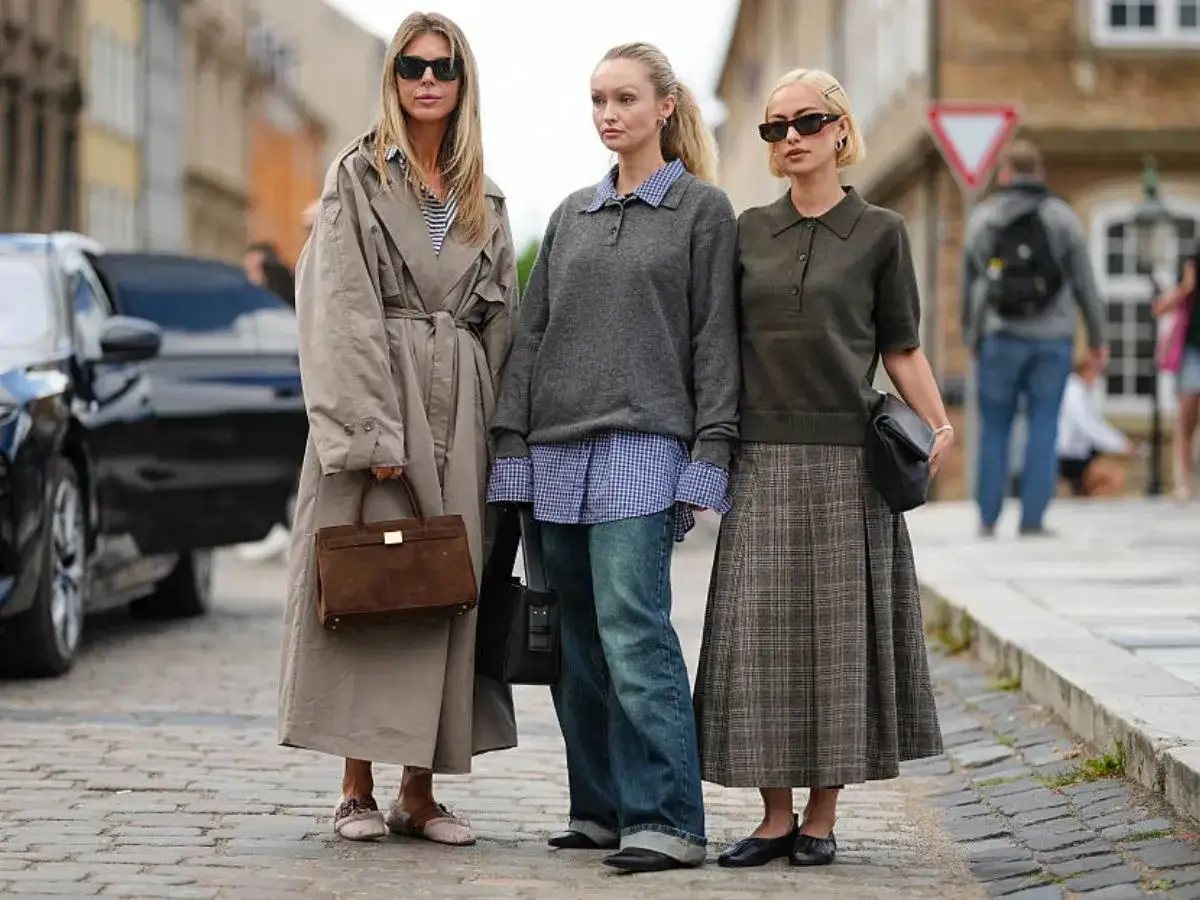 Trzy kobiety prezentują stylowe ootd: beżowy trencz, szary sweter z koszulą i jeansy, oraz zielony sweter z koszulą i spódnicą w kratę.