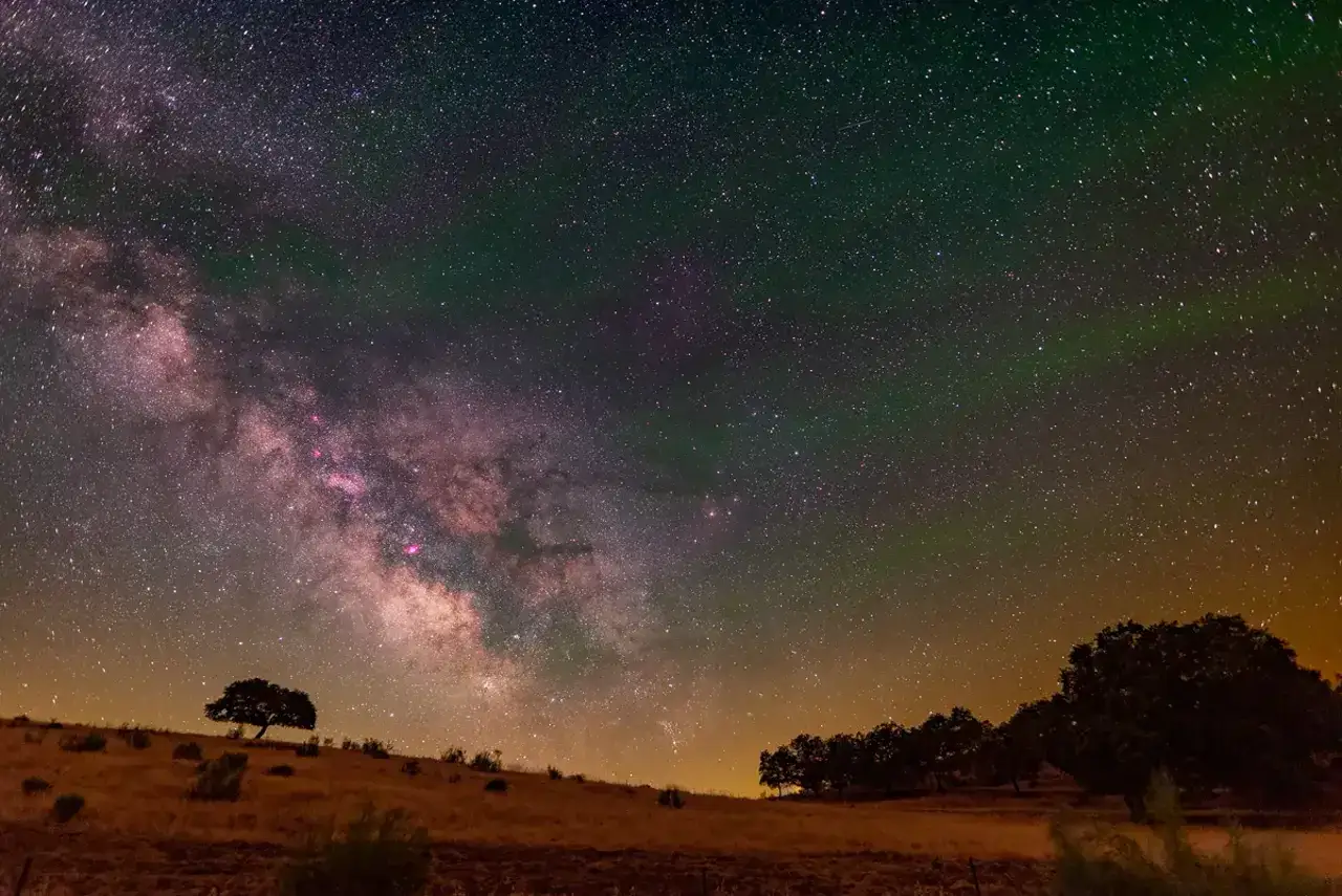 Paisaje nocturno en una reserva starlight. La V&iacute;a L&aacute;ctea cruza el cielo estrellado sobre colinas y &aacute;rboles silueteados.
