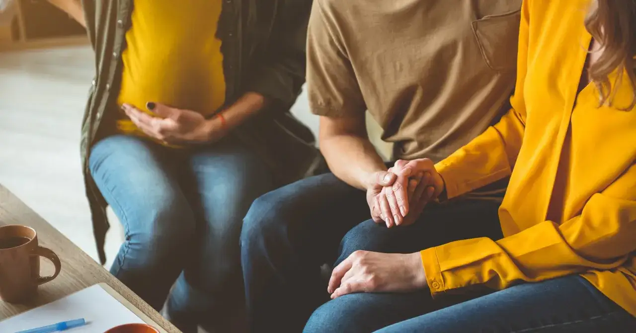Ciężarna kobieta, jej partner i surogatka trzymają się za ręce, wspierając się nawzajem w tej wyjątkowej podróży.