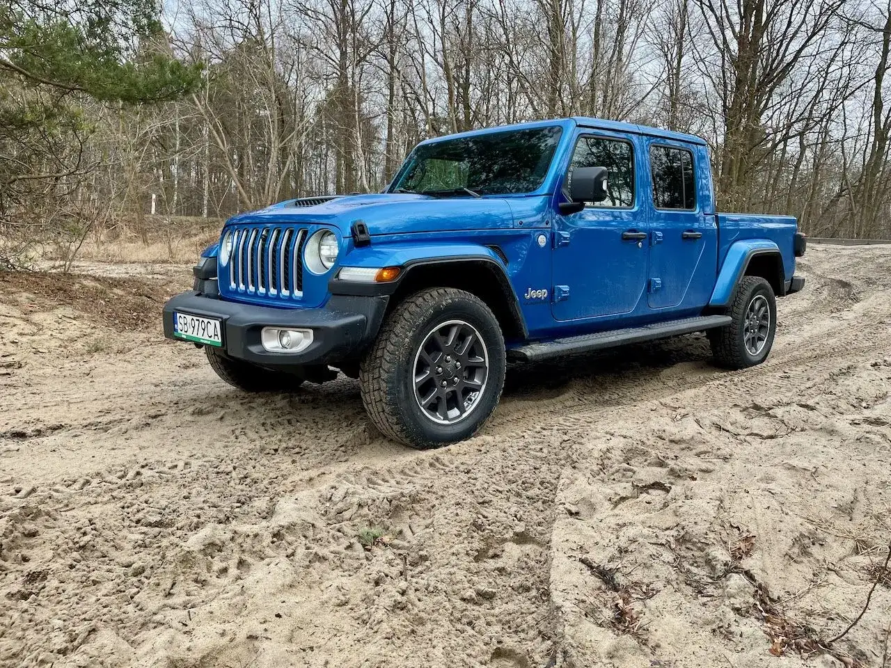 Niebieski jeep pickup na piaszczystej drodze w lesie. Gotowy na przygodę.