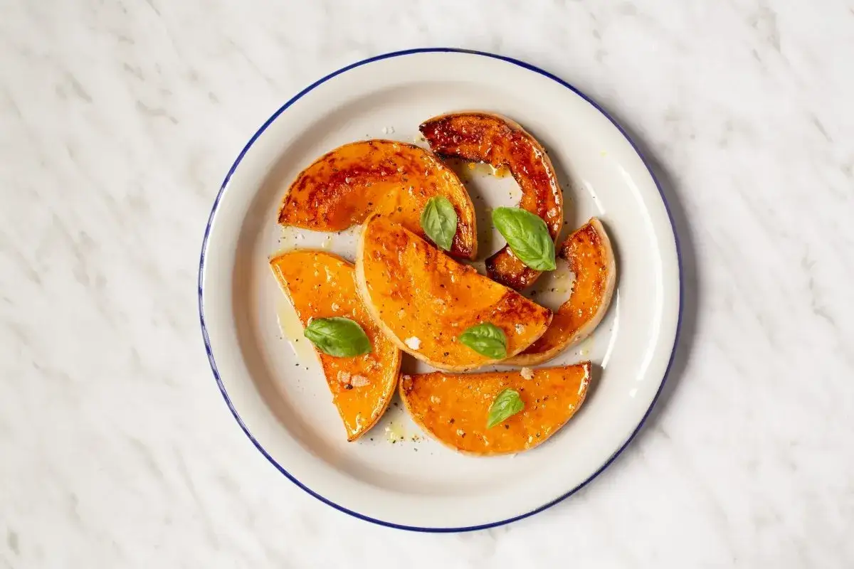 Rodajas de calabaza al horno, glaseadas y con hojas de albahaca fresca, servidas en un plato blanco con borde azul.