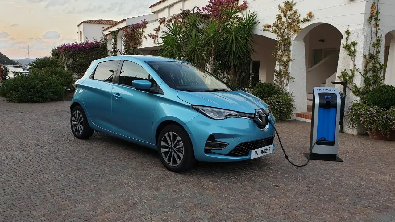 Niebieski Renault Zoe ładuje się przy stacji ładowania na tle śródziemnomorskiej willi.