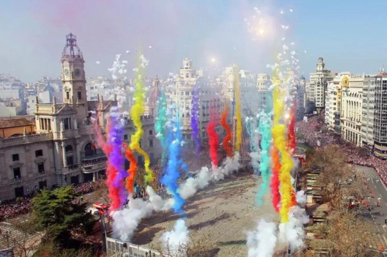 Explosión de color y humo en la mascletà hoy. Multitud celebra en la plaza ante edificios históricos.