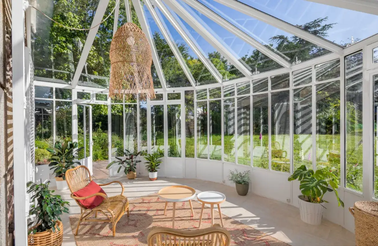 Un bel aménagement de véranda baigné de lumière, avec des meubles en rotin, des plantes vertes et une vue sur le jardin.