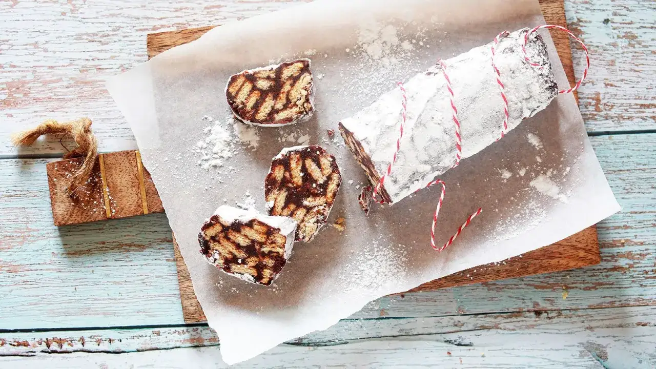 Salame al cioccolato pronto da gustare, con biscotti e cacao, spolverato di zucchero a velo.