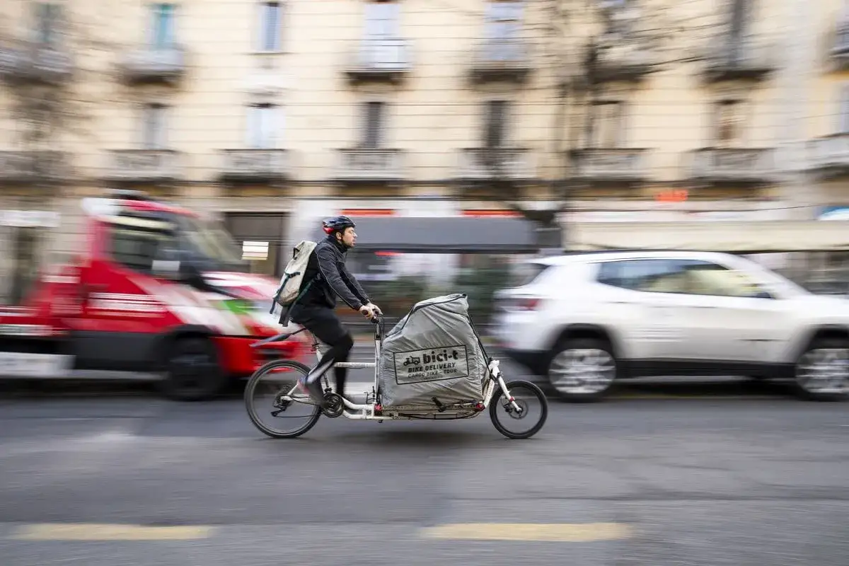 Corriere in bici cargo sfreccia in città, forse è presto, chissà a che ora iniziano a lavorare i corrieri per le consegne.