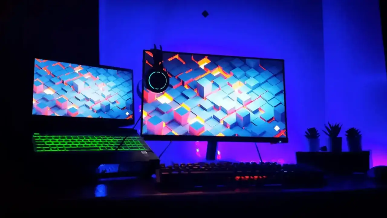 Gaming-Setup mit Laptop und externem Monitor, beleuchtet von blauer LED-Hintergrundbeleuchtung. Der Laptop hat eine grüne Tastatur und einen HDMI-Anschluss.
