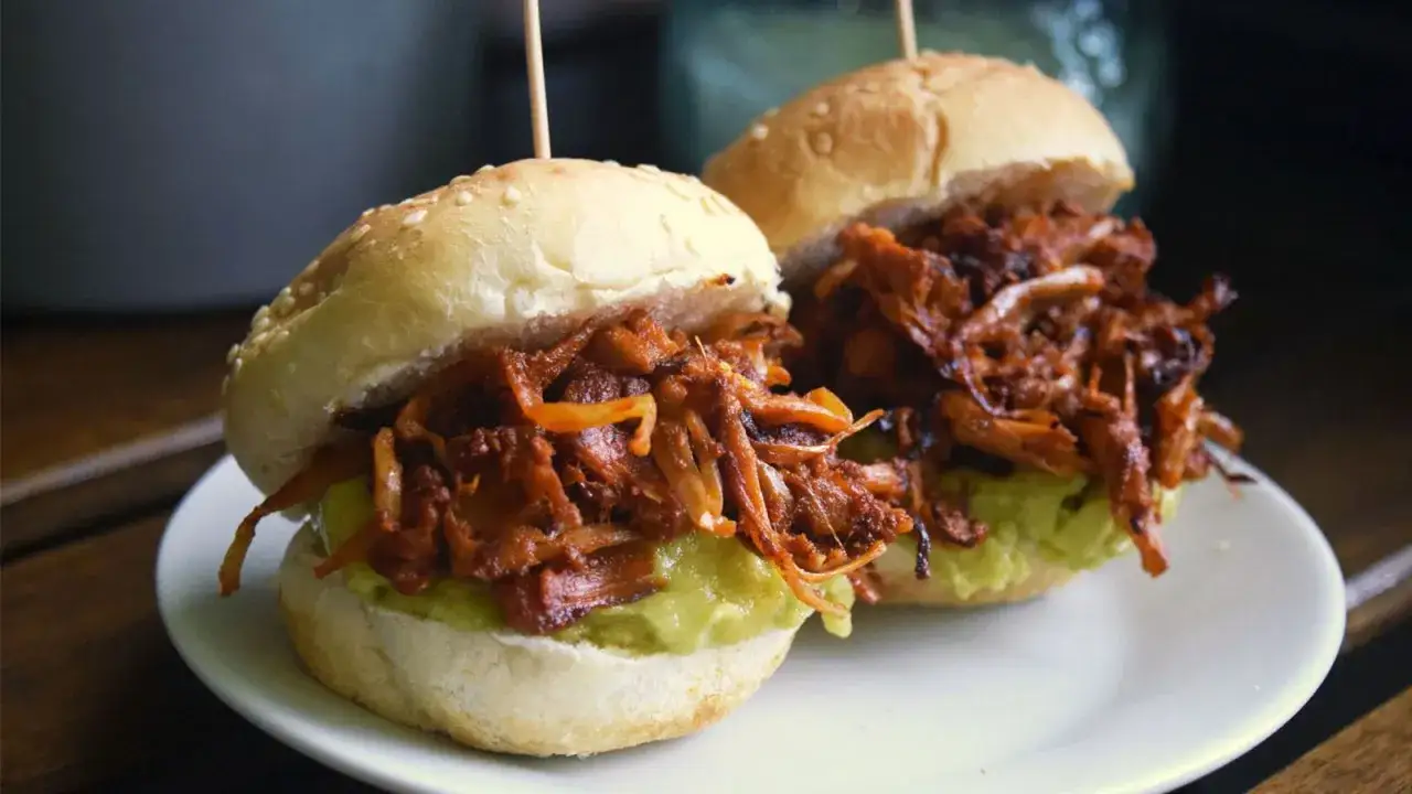Dos mini hamburguesas con pulled pork vegano jugoso y aguacate cremoso sobre panecillos con sésamo.