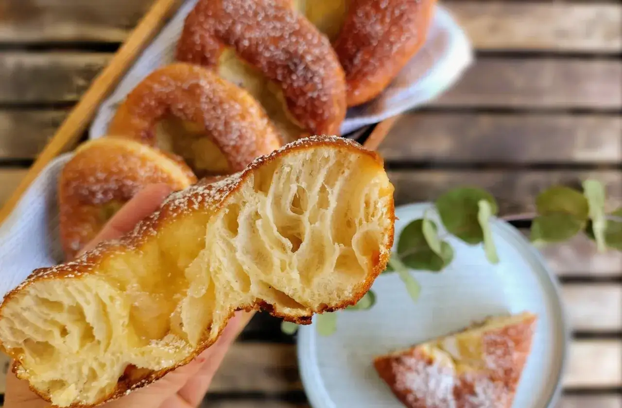 Ein handgehaltener, aufgeschnittener Krapfen aus Franken mit luftiger Krume, bestreut mit Puderzucker. Im Hintergrund weitere Krapfen im Korb.
