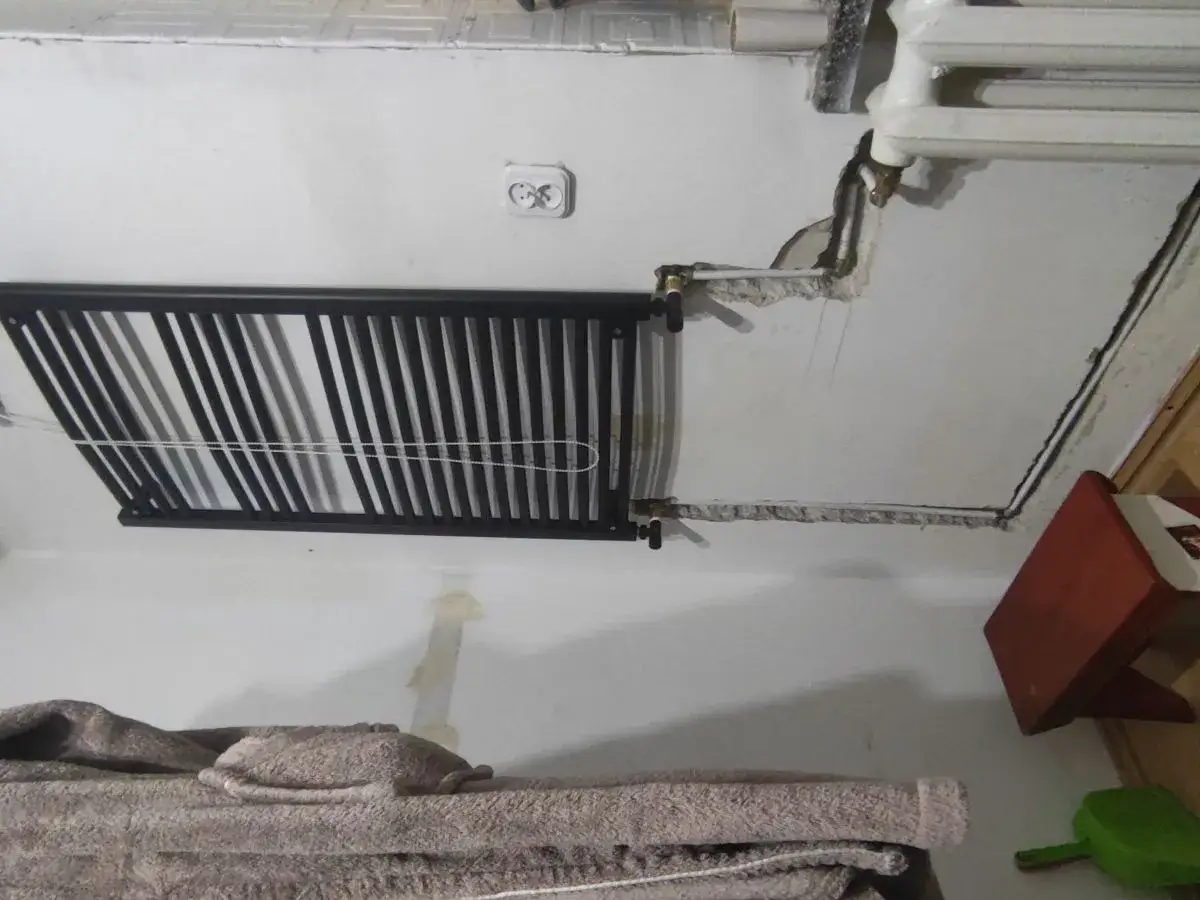 Przedstawia jak podłączenie grzejnika łazienkowego do starej instalacji wymaga prac remontowych. Widać czarny grzejnik, rury i fragment starego grzejnika.