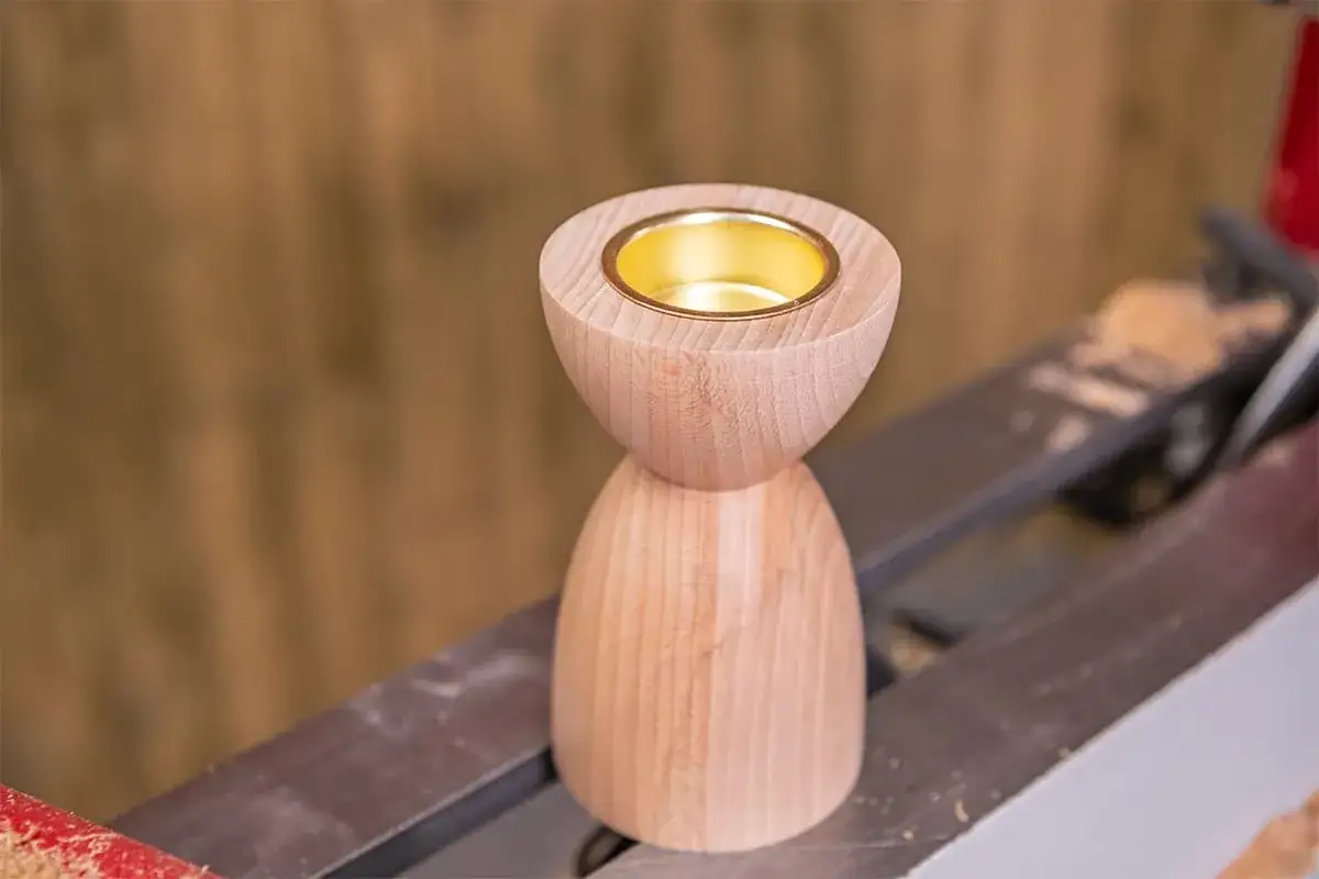 Objet à faire au tour à bois : un bougeoir en bois clair avec un insert doré.