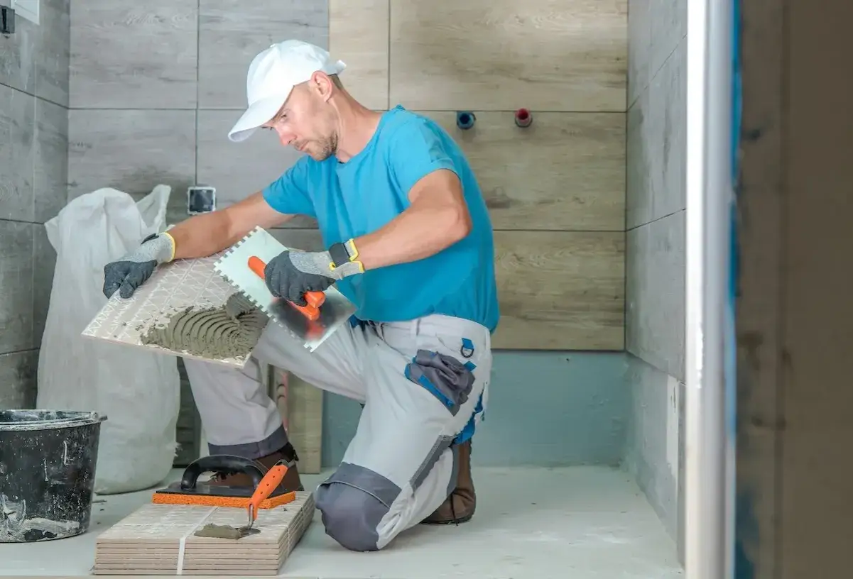 Remont łazienki: pracownik nakłada klej na płytkę ceramiczną.