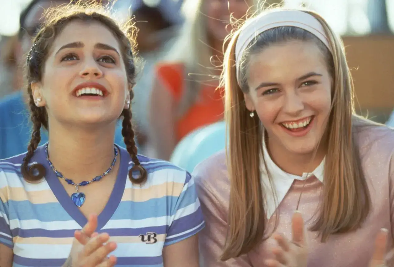 Brittany Murphy i Alicia Silverstone w filmach, dwie młode dziewczyny śmieją się i klaszczą w dłonie, ubrane w kolorowe stroje.
