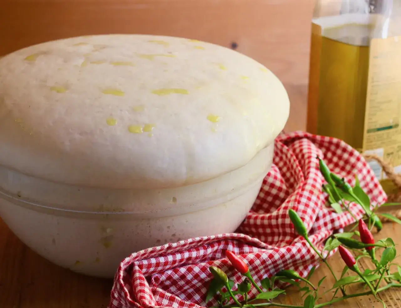 Impasto lievitato per pizza con lievito di birra, pronto per essere infornato. Olio d'oliva e peperoncini completano la scena.