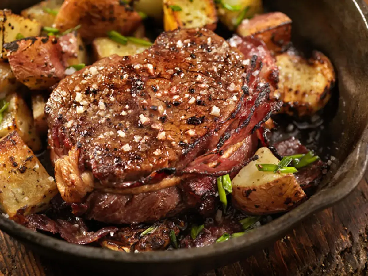 Ein saftiges Schweinesteak im Backofen, umh&uuml;llt von knusprigem Speck, serviert mit goldbraunen Kartoffelspalten. Perfekt gegart, ohne vorheriges Anbraten.